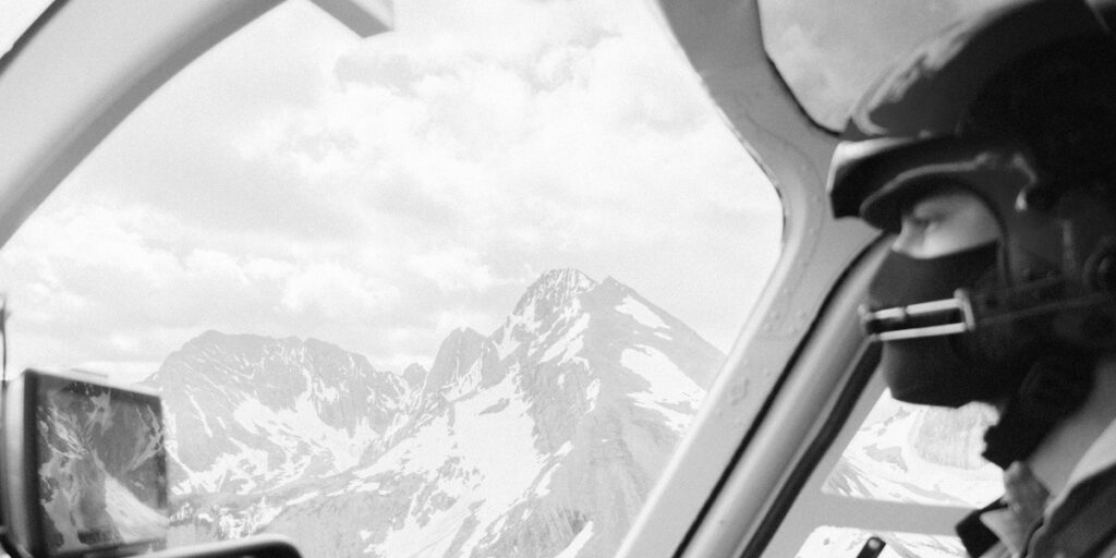 Helicopter pilot in cockpit flying over snow-covered mountains
